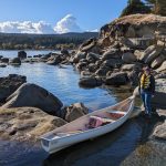 Sarah Glen next to a canoe pulled up on the rocky shore.